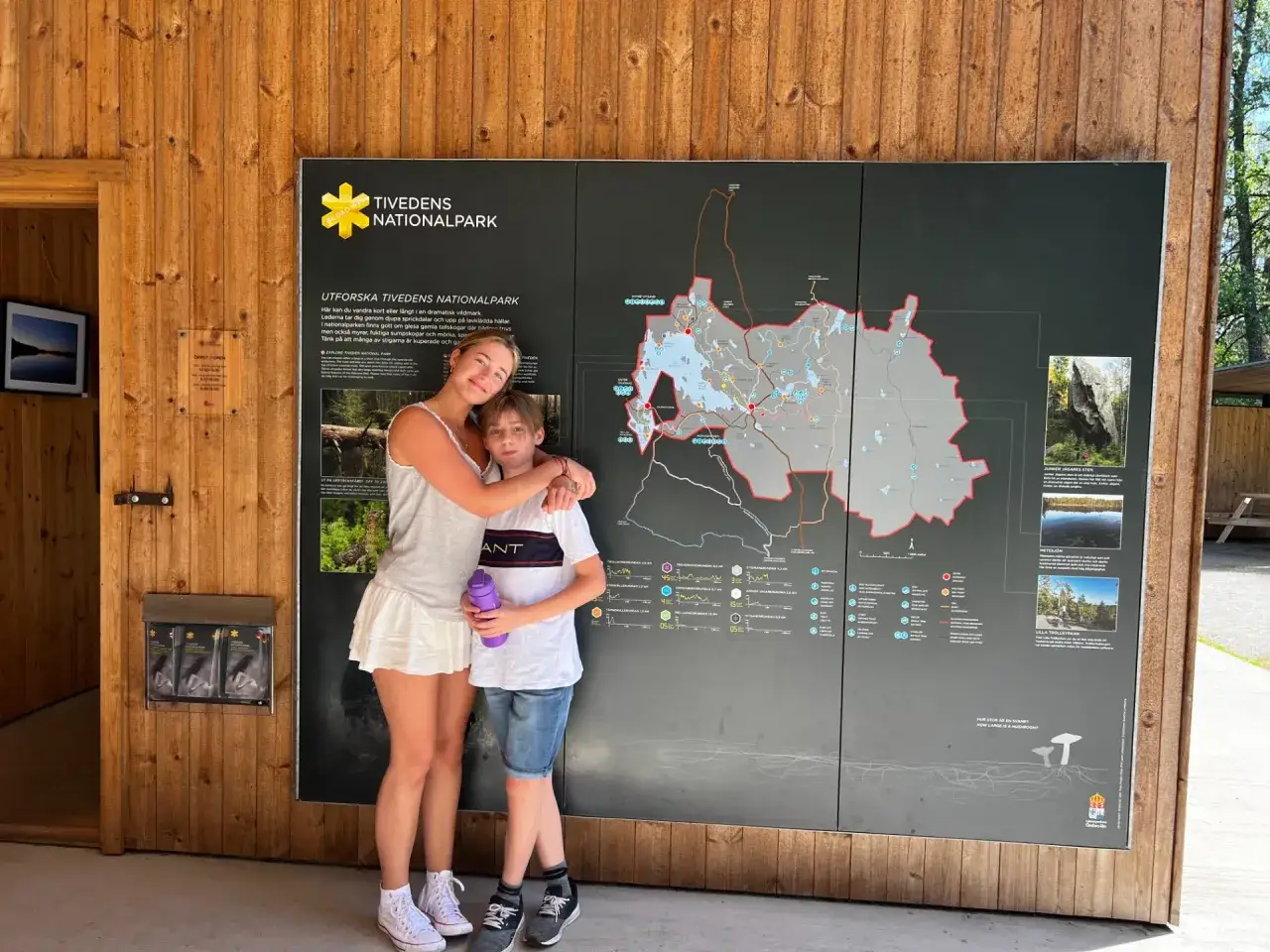 Tv&aring; barn, en flicka och en pojke, st&aring;r framf&ouml;r en karta &ouml;ver Tivedens nationalpark.