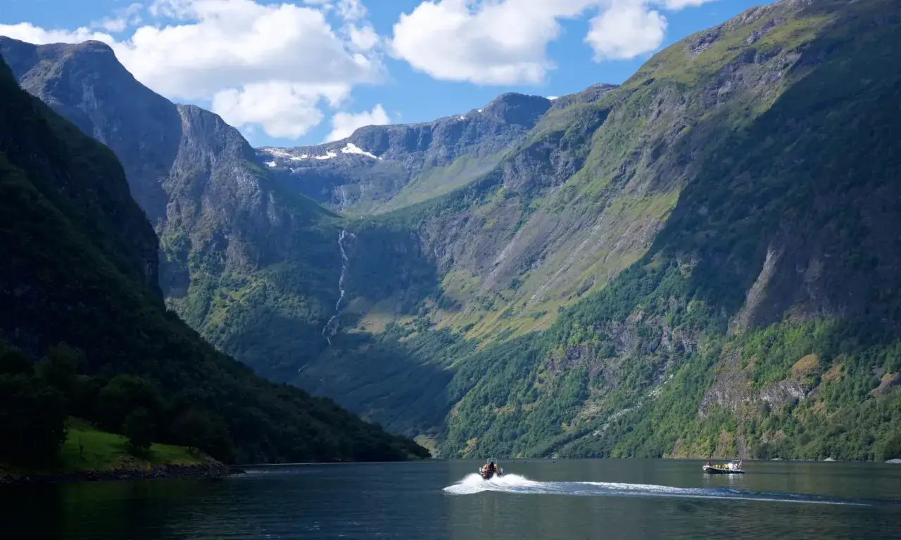 En b&aring;t susar fram p&aring; en fjord i Norge, omgiven av dramatiska berg och gr&ouml;nska. Kanske &auml;r de ute och fiska i norge.