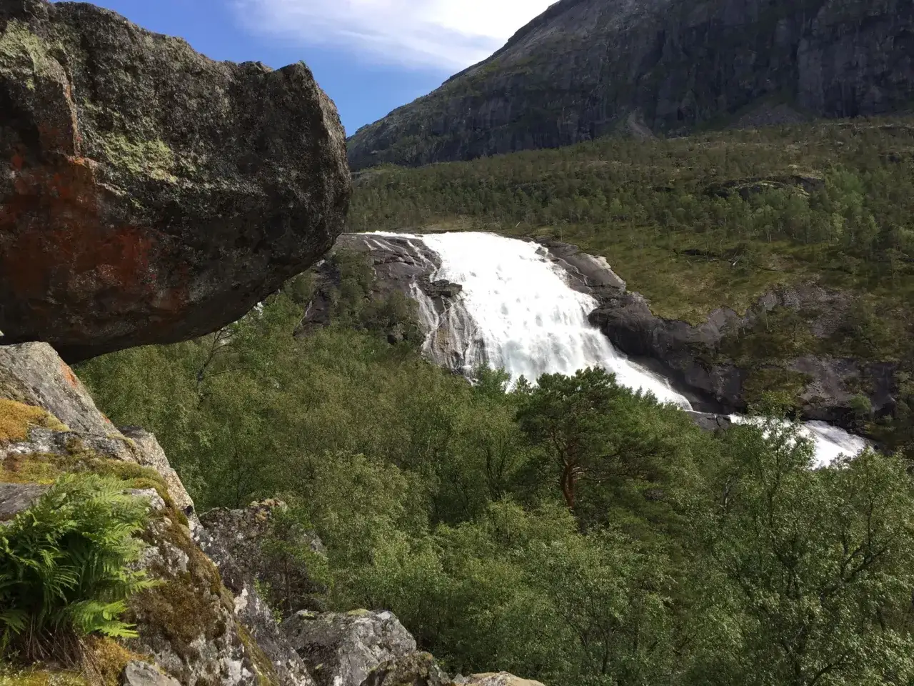 Vandring Hardangervidda: en m&auml;ktig forsande vattenfall omgiven av gr&ouml;nskande skog och dramatiska berg.