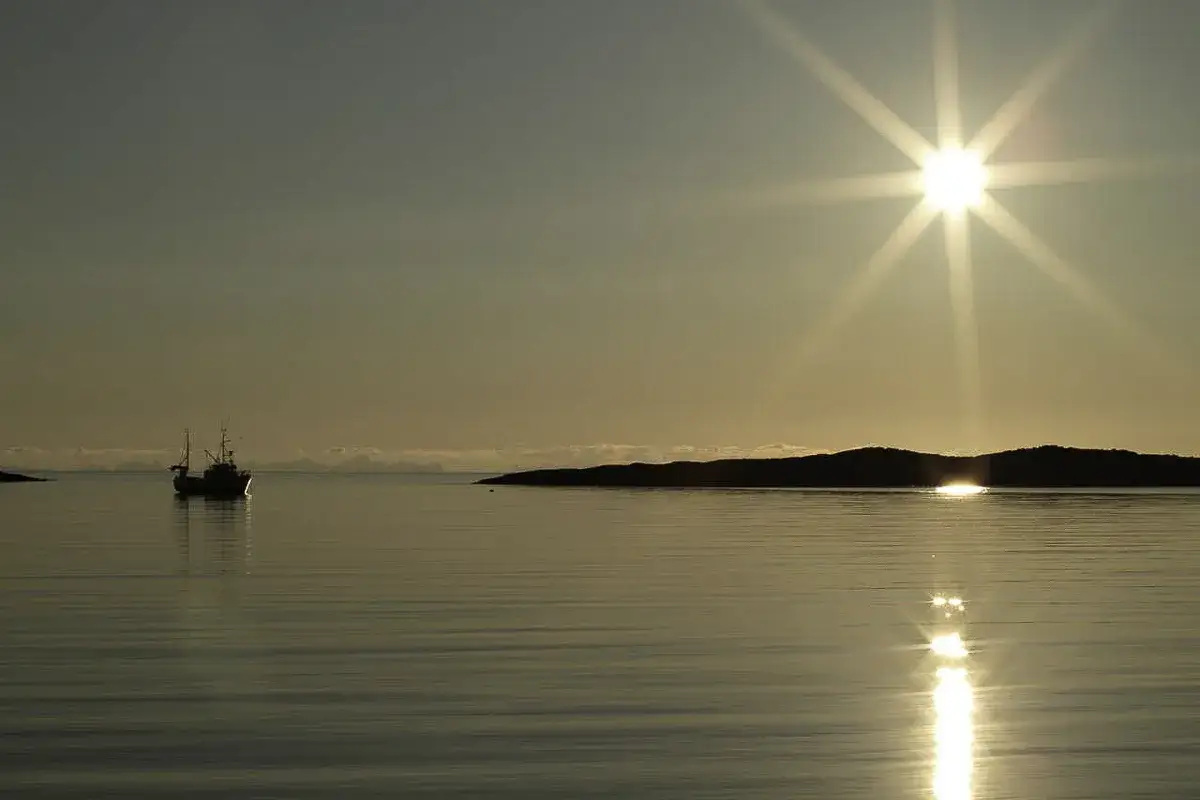 En fiskebåt seglar i solnedgången utanför Bodo, Norge. Solen strålar över det lugna vattnet.