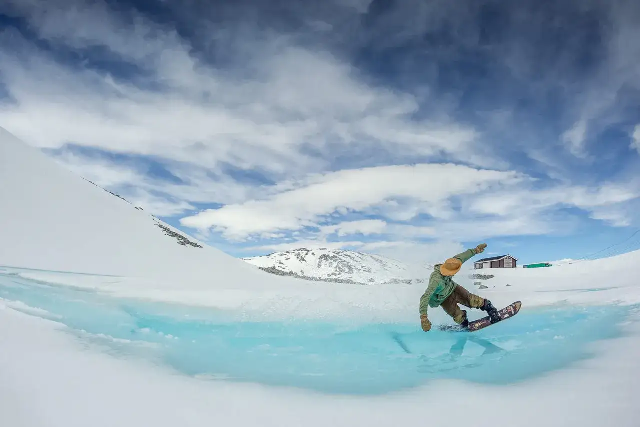 En snowboard&aring;kare g&ouml;r en sv&auml;ng &ouml;ver en isig sj&ouml; i Norge, en perfekt dag f&ouml;r sommarskid&aring;kning.