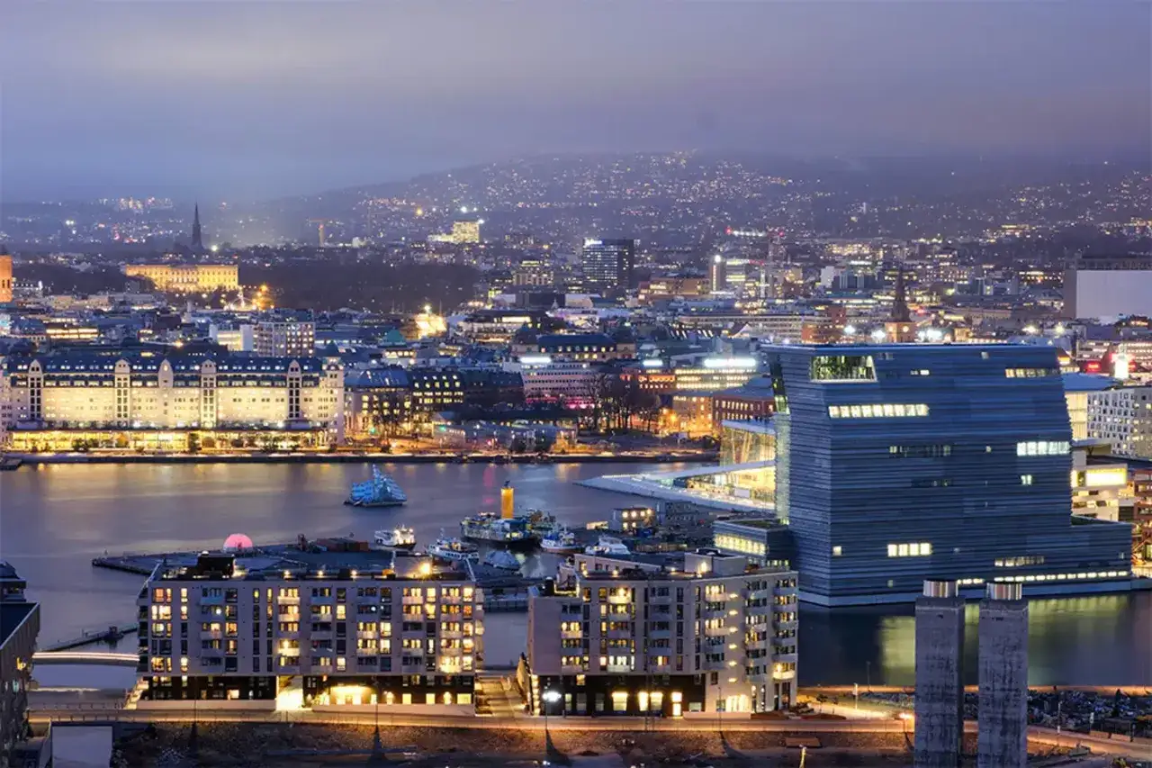 Fakta om Oslo: En stad vid vattnet med moderna byggnader och upplysta fönster, som speglar sig i det mörka vattnet.