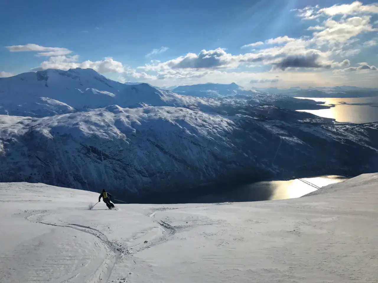 En skidåkare njuter av fantastisk narvik skidåkning i ett snöigt berglandskap med en glittrande fjord i bakgrunden.