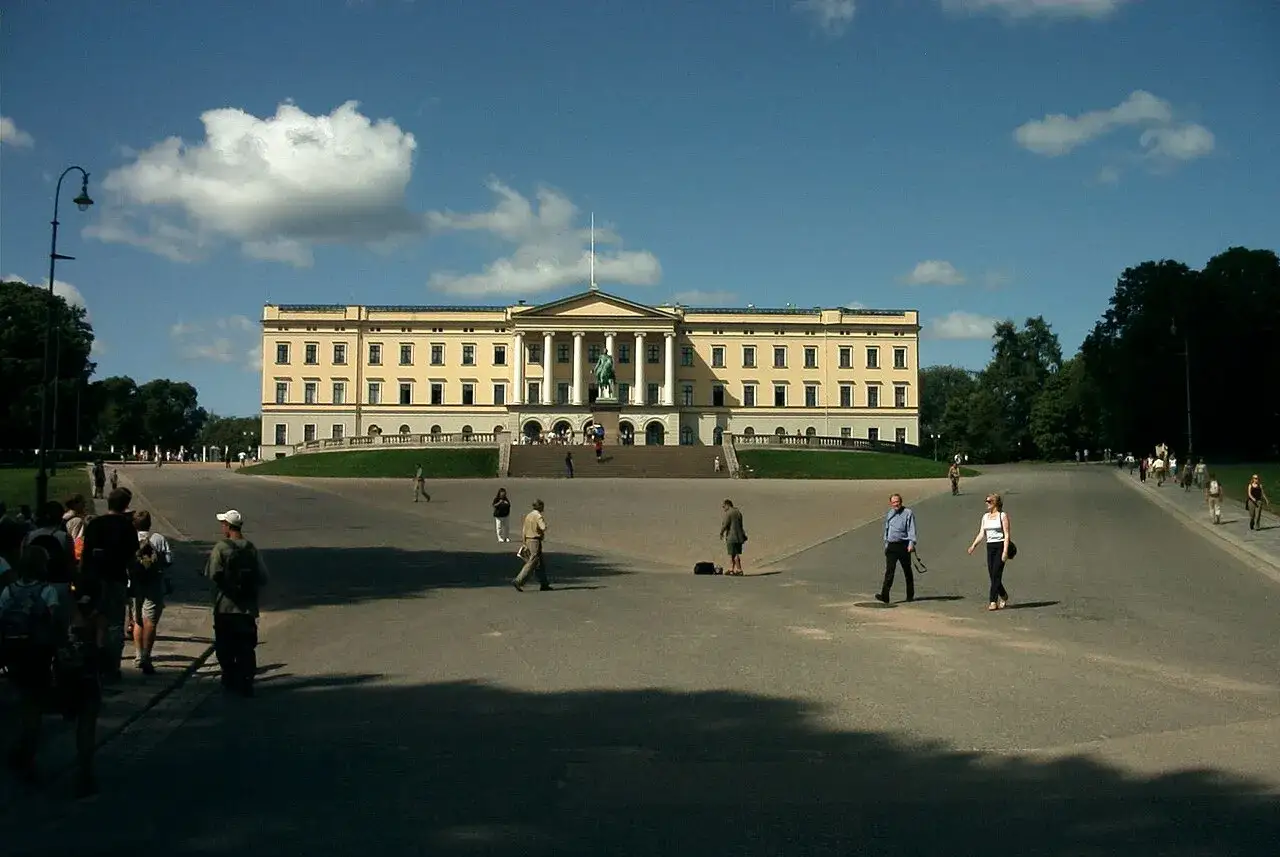 Det gula Oslo slott med sin imponerande fasad och staty framför. Människor promenerar på den stora, solbelysta ytan.