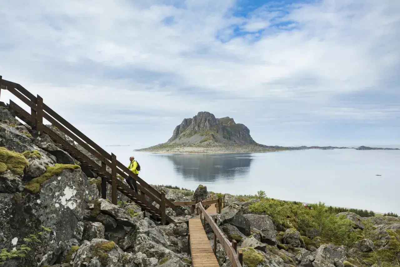 Vandrare på trappa vid havet på Vega Norge, med en imponerande klippö i bakgrunden.