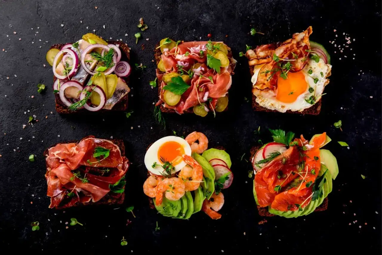 Sex olika varma mackor i ugn med olika p&aring;l&auml;gg: sill, prosciutto, &auml;gg med bacon, r&auml;kor med avokado och lax med avokado.