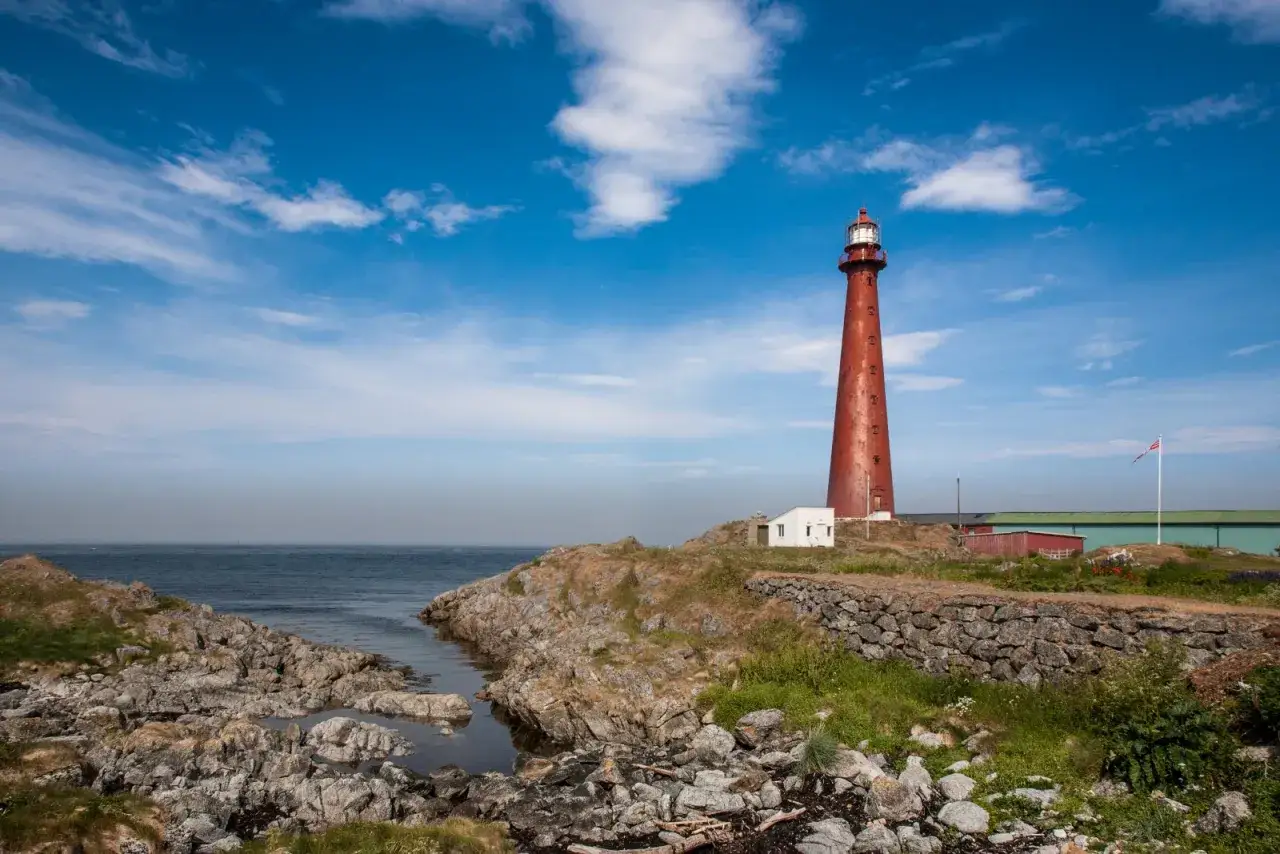 Rött fyrtorn vid havet på Andenes, Norge. En vit byggnad står vid dess fot.