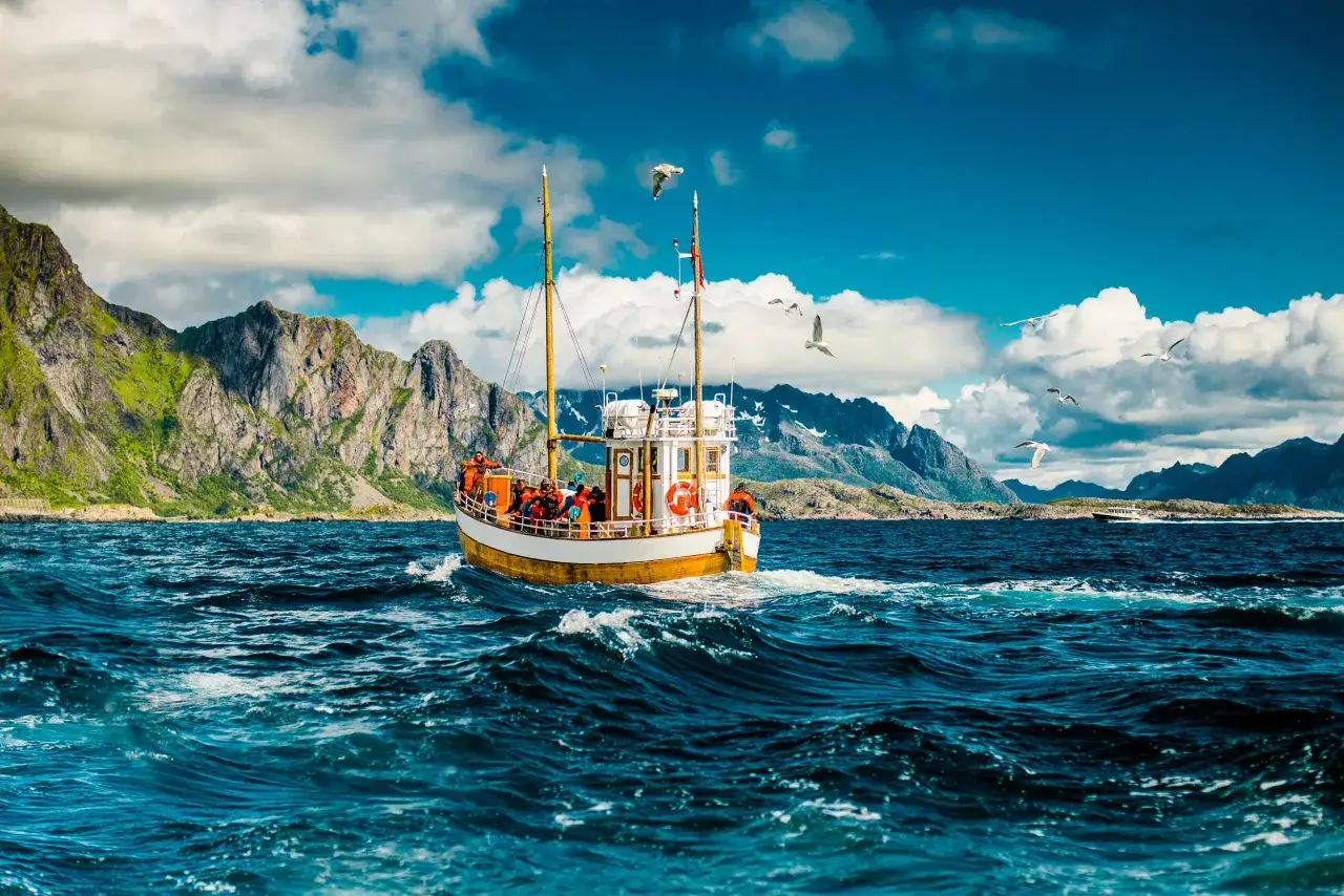 B&aring;t med passagerare p&aring; havet i Norge, med dramatiska berg i bakgrunden. En perfekt dag f&ouml;r havsfiske i Norge.