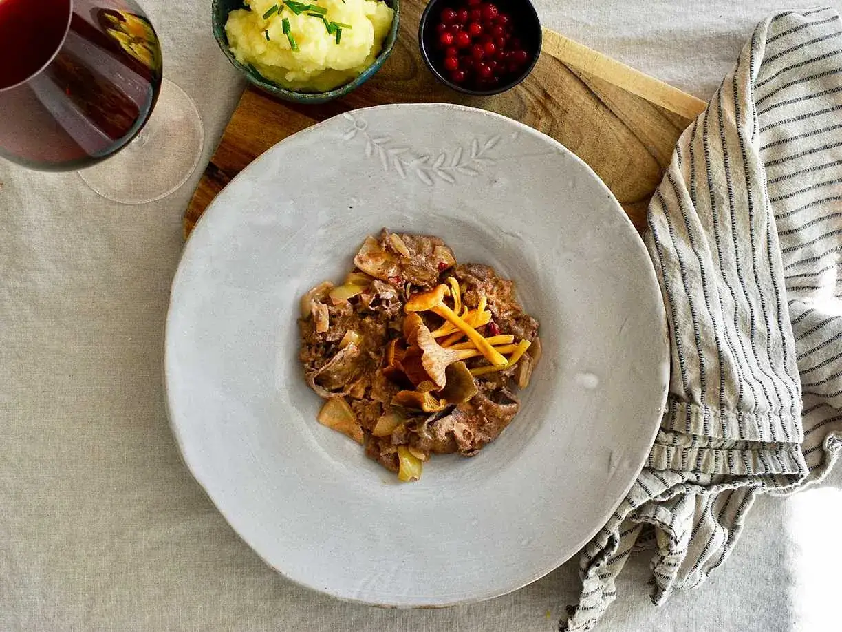 En tallrik med renskav, svamp och gul lök. Tillbehör är potatismos, lingon och ett glas rödvin. Ett perfekt renskav recept för en mysig middag.