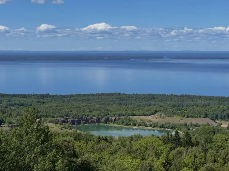 Vacker utsikt över en sjö och en grönskande skog. En liten sjö med klippor syns i mitten, en del av **Götaleden etapp 7**.
