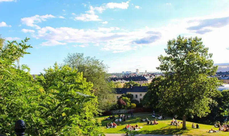 En solig dag med en härlig piknik i parken. Människor njuter av gräset och utsikten över staden.